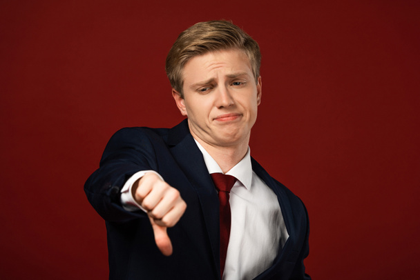 nespokojený muž ukazující palec dolů na červeném pozadí - Fotografie, Obrázek