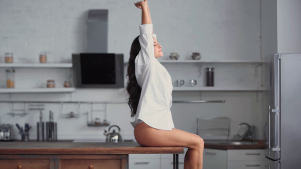 glimlachende vrouw zittend op tafel en stretching in de keuken  - Video