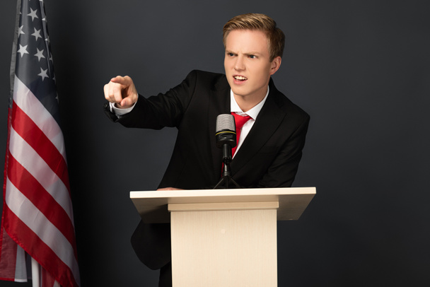 homme émotionnel en colère pointant du doigt sur tribune avec drapeau américain sur fond noir
 - Photo, image