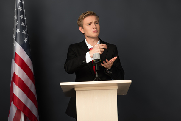 Emotionaler Mann spricht auf Tribüne mit amerikanischer Flagge auf schwarzem Hintergrund - Foto, Bild