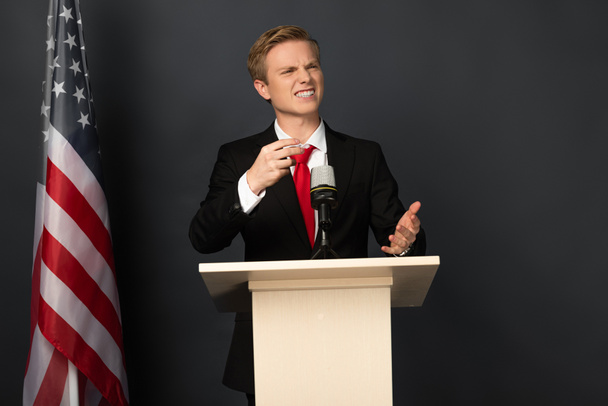 tunteellinen mies puhuu ja irvistelee tribuunissa Amerikan lippu mustalla taustalla
 - Valokuva, kuva