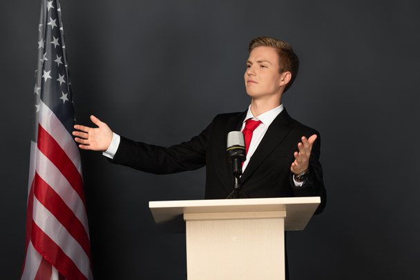 emotivní muž gestikuluje na tribuně s americkou vlajkou na černém pozadí - Fotografie, Obrázek