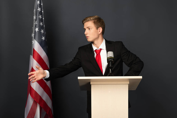 hombre emocional hablando y haciendo gestos en tribuna con bandera americana sobre fondo negro
 - Foto, imagen