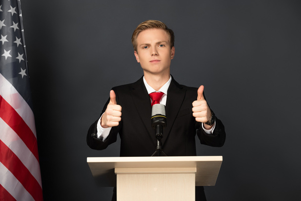  emotional man showing thumbs up on tribune with american flag on black background - Fotó, kép