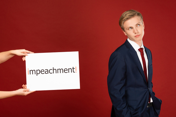 skeptical man near white card with impeachment lettering on red background - Valokuva, kuva