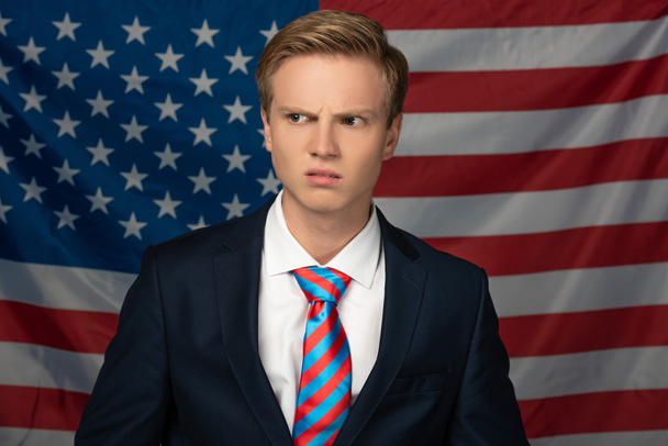 растерянный мужчина, отводящий взгляд на фоне американского флага
 - Фото, изображение