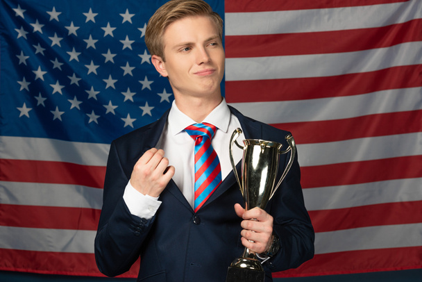 Человек держит золотой кубок на фоне американского флага
 - Фото, изображение
