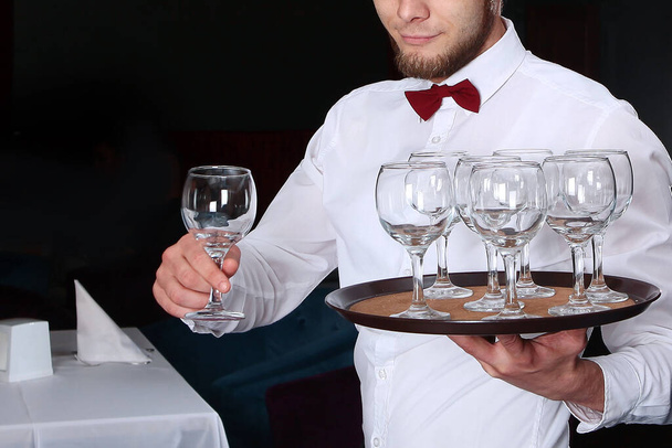 Młody kelner podaje kieliszki do wina. Zdjęcie bez twarzy we wnętrzu restauracji. - Zdjęcie, obraz
