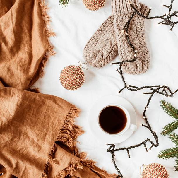 Новорічна / Різдвяна композиція. В'язані рукавички, чашка для кави, гірлянда, ялинкові гілки, різдвяні сукні, імбирні пледи на білій ковдрі. Плоский ліжко, вид зверху прикрашений святковим фоном
. - Фото, зображення