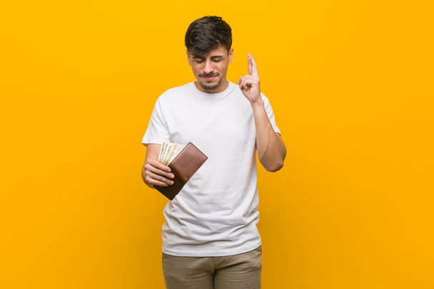 Young hispanic man holding a wallet crossing fingers for having luck - Φωτογραφία, εικόνα