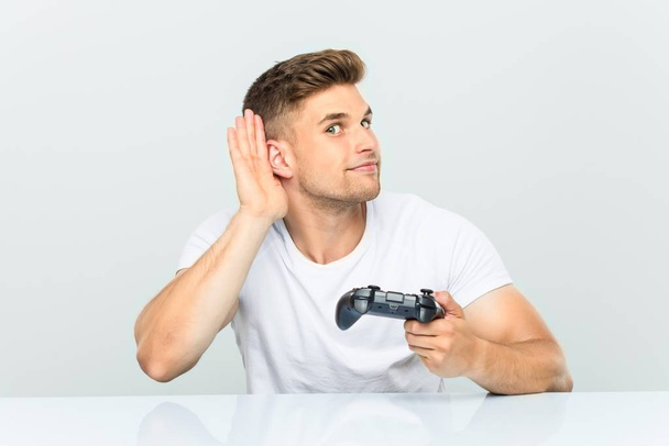 Молодий чоловік тримає контролер гри, намагаючись слухати плітки
. - Фото, зображення