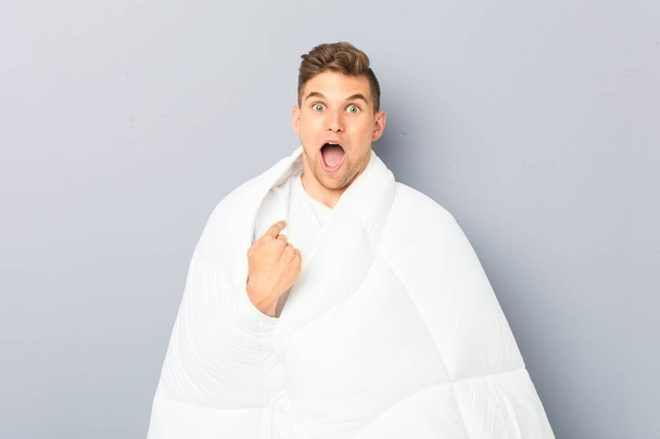 Young man holding a nordic duvet surprised pointing at himself, smiling broadly. - Photo, Image