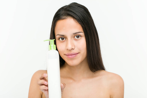 Close-up de uma bela e natural hispânica jovem segurando uma garrafa de creme hidratante
 - Foto, Imagem