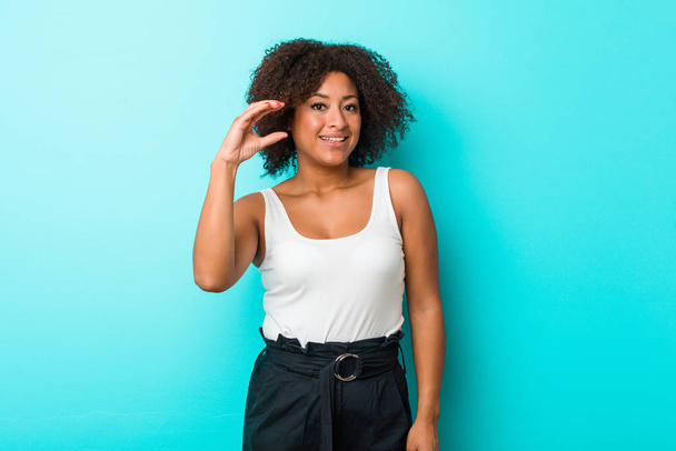 Joven mujer afroamericana sosteniendo algo poco con los dedos índice, sonriente y confiada
. - Foto, Imagen