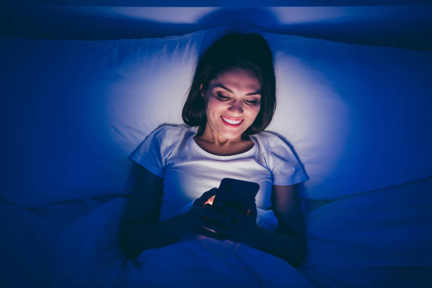 Close-up top above high angle view portrait of her she nice attractive cheerful cheery girl lying in bed chatting online with boyfriend using 5g app date service in dark blue room house flat - 写真・画像