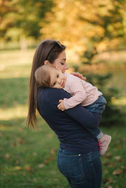 Portrait of beautiful family in the park. Mom and daughter togehter in autumn. Beautiful ten month baby on mothers hands - 写真・画像