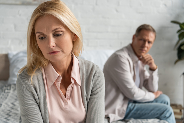 Selective focus of worried woman with husband sitting on bed - Foto, afbeelding