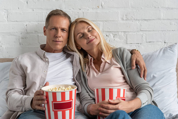 Couple holding popcorn buckets and sitting on bed - Foto, afbeelding