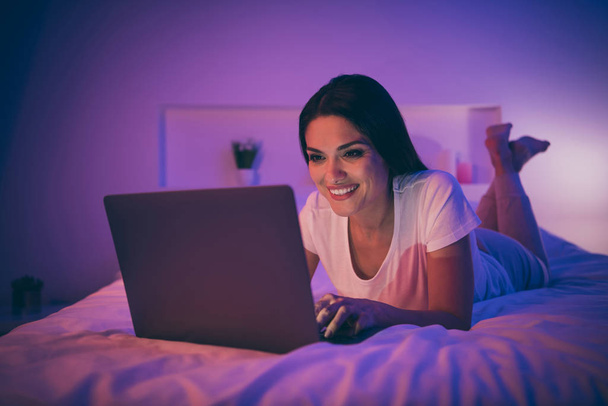 Portrait of her she nice attractive lovely cheerful cheery mature girl lying on bed using laptop chatting with boyfriend enjoying leisure at night light room house flat illumination - 写真・画像