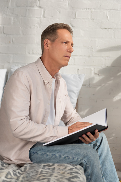 Un hombre reflexivo sosteniendo un cuaderno y mirando a la cama
 - Foto, imagen