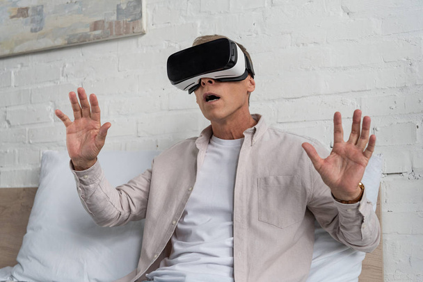 Exited man in virtual reality headset op bed - Foto, afbeelding