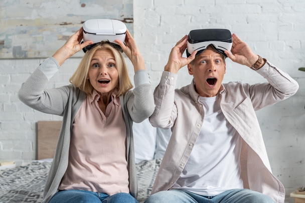 Shocked couple with virtual reality headsets looking at camera on bed - Foto, imagen
