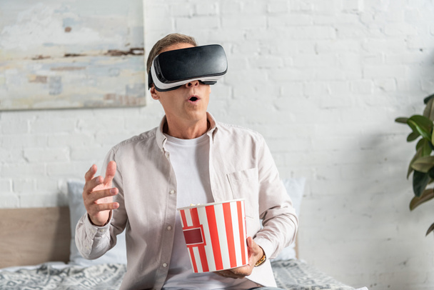 Вышедший мужчина в гарнитуре виртуальной реальности с попкорном на кровати
 - Фото, изображение
