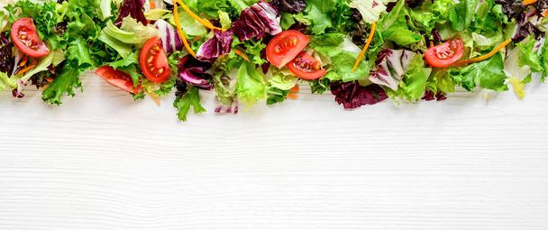 Mixed fresh salad leaves and vegetables on white wooden table. Background, border, frame, website header - Photo, Image