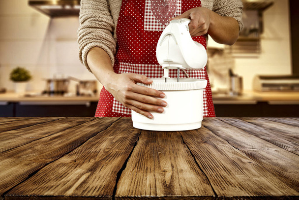 Woman in red apron with white mixer in kitchen and wooden desk top space for products and decorations. - Fotoğraf, Görsel
