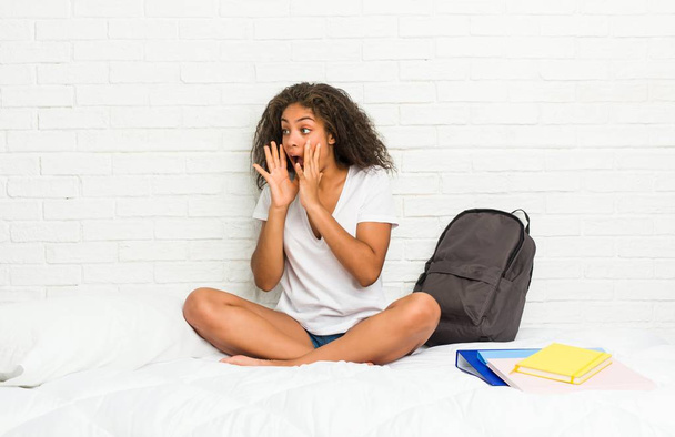 Jeune étudiante afro-américaine sur le lit crie fort, garde les yeux ouverts et les mains tendues
. - Photo, image