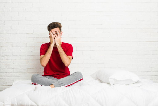 Jeune adolescent étudiant homme sur le lit cligner des doigts effrayé et nerveux
. - Photo, image