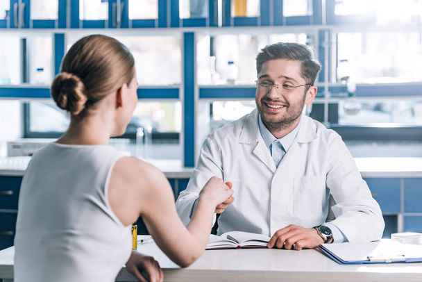 selective focus of happy doctor in glasses shaking hands with woman  - Photo, Image