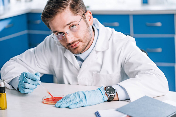 handsome immunologist holding pipette with red liquid in lab  - Photo, Image
