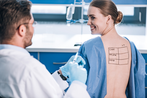 selective focus of happy patient with letters on marked back looking at allergist  - Foto, Imagen