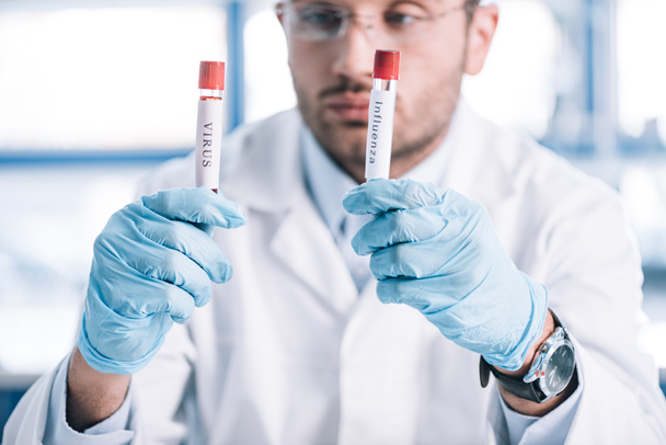 selective focus of bearded immunologist holding test tubes with letters  - Foto, Bild