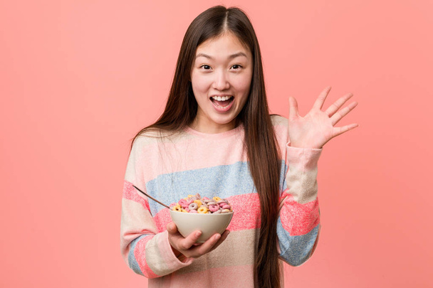 Young asian woman with a cereal bowl celebrating a victory or success - Φωτογραφία, εικόνα