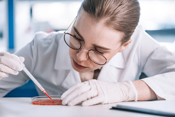 selective focus of attractive immunologist holding pipette with red liquid  - Fotografie, Obrázek