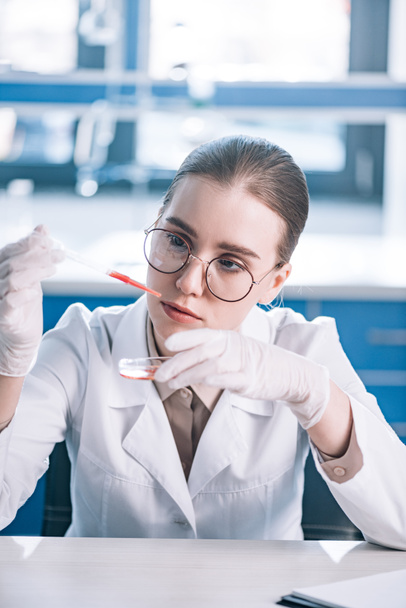 selective focus of beautiful immunologist holding pipette with red liquid in laboratory  - Fotografie, Obrázek