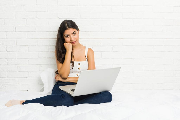 Mujer árabe joven trabajando con su portátil en la cama que se siente triste y pensativo, mirando el espacio de copia
. - Foto, imagen