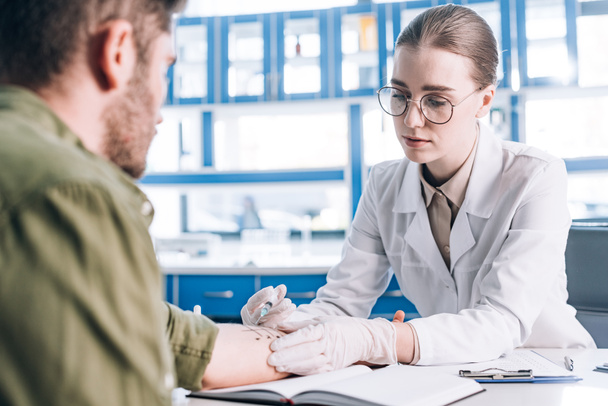 Selektiver Fokus attraktiver Allergologe hält Spritze in der Nähe von Mann in Klinik  - Foto, Bild