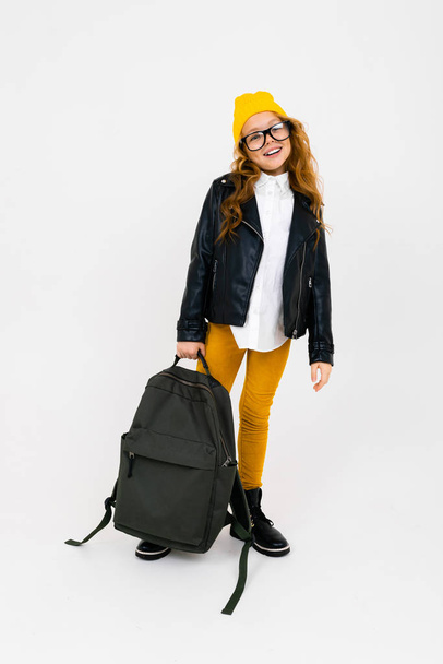 cool little girl in laser jacket posing with backpack in studio on light background  - Φωτογραφία, εικόνα