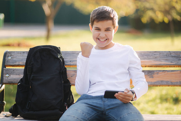 10代の男の子は学校でのレッスンの後、公園で彼のスマートフォンでオンラインゲームをプレイ - 写真・画像