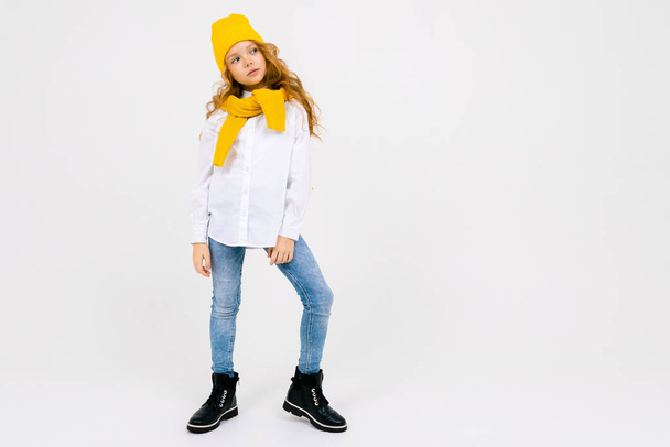 Porträt eines modischen netten kleinen Mädchens, das vor hellem Hintergrund mit gelbem Hut und Schal posiert  - Foto, Bild