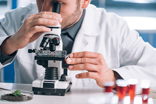 cropped view of bearded biochemist looking through microscope in laboratory  - Zdjęcie, obraz