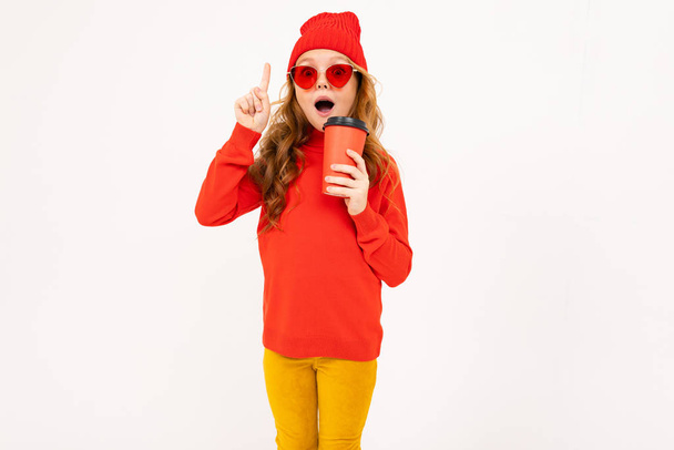 jolie fille en lunettes rouges posant avec des écouteurs et tenant tasse en papier en studio sur fond clair
  - Photo, image