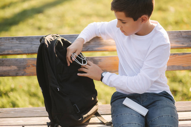 Przystojny nastolatek bierze z plecaka powerbark za ładowanie smartfona. Cute boy w parku w czasie jesieni - Zdjęcie, obraz