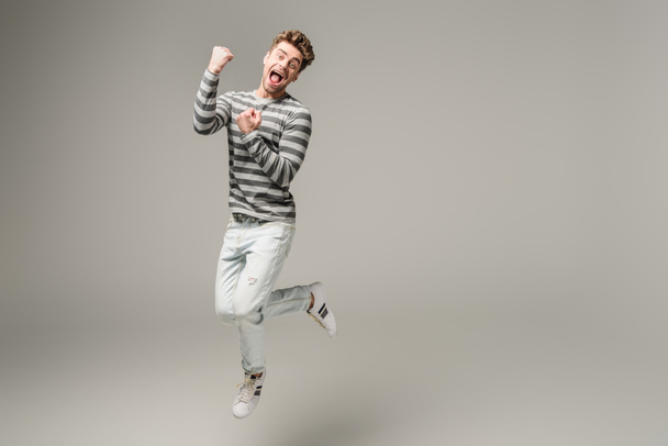 excited screaming man jumping and cheering on grey - Photo, Image