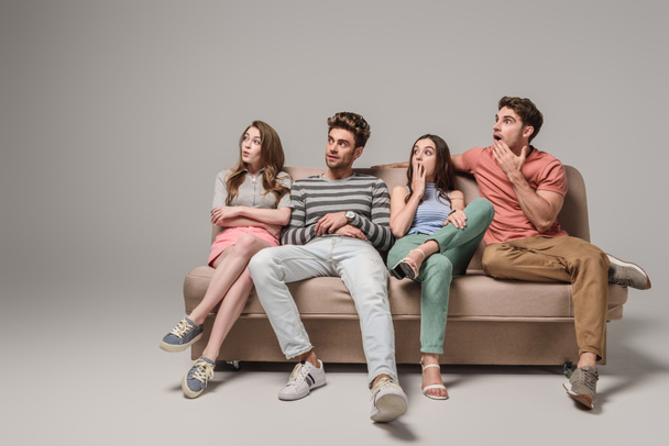 shocked young friends sitting together on sofa on grey  - Фото, зображення