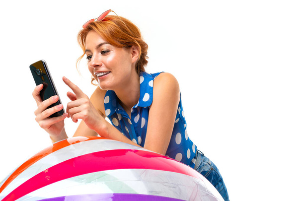 νεαρή κοκκινομάλλα γυναίκα ποζάρουν με κινητό τηλέφωνο και φουσκωτή μπάλα λευκό φόντο   - Φωτογραφία, εικόνα