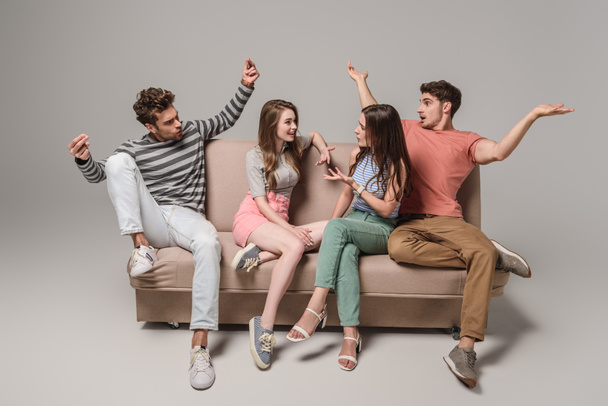 emotional young friends talking and sitting on sofa on grey  - Foto, Bild